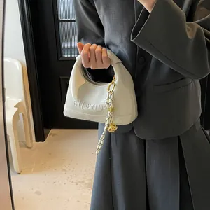 Detail of off-white dumpling bag with embossed sensitia text and golden charm