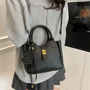 Détail du sac à main en cuir grainé noir avec finitions dorées et breloque petit chien