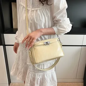 Detail of cream crossbody bag featuring silver turn-lock and woven handle texture