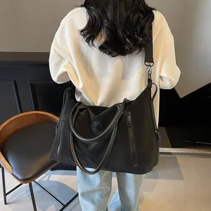 Rear view of model carrying a large black waterproof nylon travel tote with leather handles