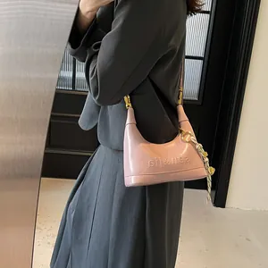 Detail view of the pink faux leather shoulder bag with glossy finish and braided ornament