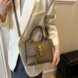 Sac seau minimaliste en cuir grainé taupe avec fermoir rotatif en métal et breloque chien
