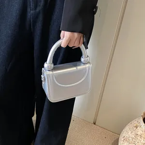Détail d'un sac à main argenté métallisé avec perles sur la poignée et design à rabat lisse