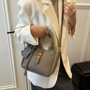 Sac seau en cuir gris grainé avec fermoir doré et breloque chien porté par un mannequin