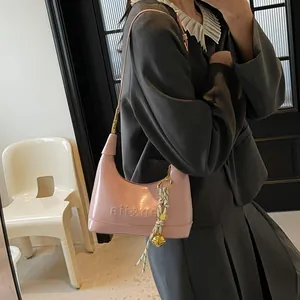 Close-up of pink glossy patent leather shoulder bag with bell charm and logo detail