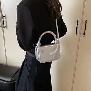 Détail d'un mini sac argenté métallisé avec poignée incurvée et finition brillante