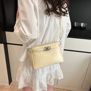 Detail view of cream Kelly style crossbody bag with silver buckle on female model
