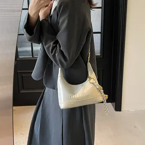 Chic beige crescent shoulder bag with glossy leather and striped scarf detail on model