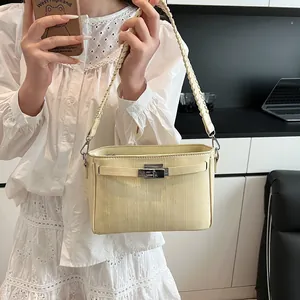 Detail of cream Kelly-style handbag showing metallic turn-lock and woven strap