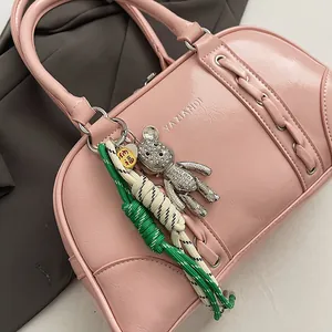 Close-up of pink glossy shoulder bag with teddy bear charm and woven rope detail