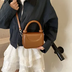 Détail d'un petit sac à main marron brillant avec poignée et finitions métalliques
