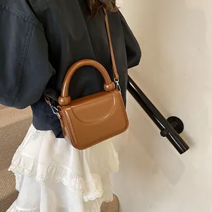 Sac à bandoulière marron en cuir verni brillant porté par un mannequin avec sangle réglable