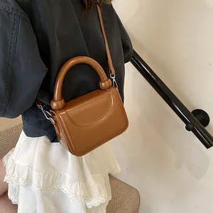 Petit sac carré marron avec poignée épaisse et bandoulière porté par un mannequin
