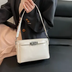 Detail of white square crossbody bag with metallic turn-lock and woven leather strap