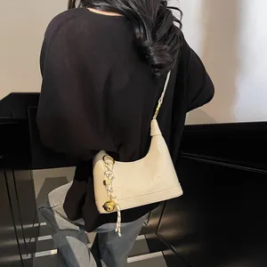 Detail of a creamy white crossbody bag featuring embossed text and a golden bell charm