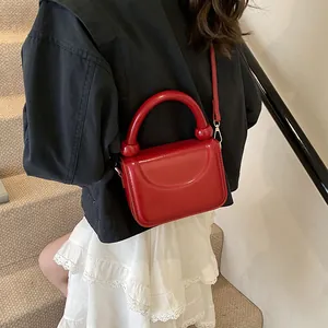 Détail du petit sac carré rouge brillant avec poignée ronde et bandoulière assortie