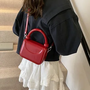 Vue détaillée du sac à main rouge en cuir verni brillant porté par un mannequin en manteau