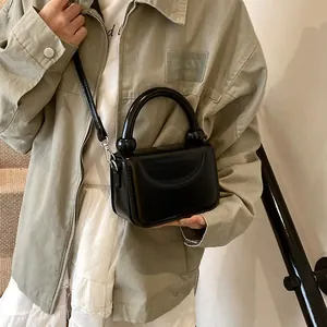 Détail d'un mini sac carré noir brillant avec une poignée épaisse et boucles argentées