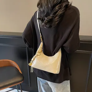 Detail of beige glossy leather shoulder bag with embossed letters and knot pendant