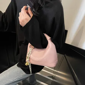 Detail of light pink crescent handbag with scarf charm and gold hardware on shoulder