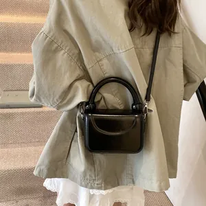 Gros plan d'un sac à main carré noir brillant avec une poignée et une bandoulière