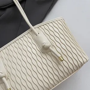 Close-up of cream shoulder bag featuring wavy texture and knotted strap with gold metal tips