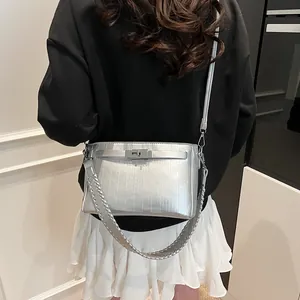 Detail of silver textured handbag with turn-lock and interchangeable woven strap on model
