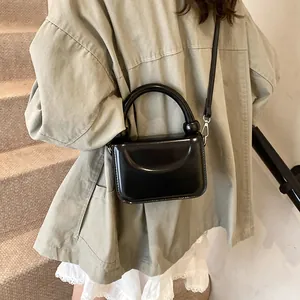 Mini sac carré noir brillant porté par un mannequin en manteau kaki et jupe en dentelle
