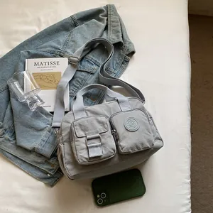 Detail view of a light grey multi-pocket nylon crossbody bag in a casual lifestyle setting