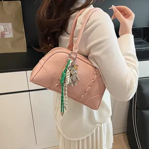 Close-up of pink Boston bag with glossy texture, metal bear charm and colorful woven ropes