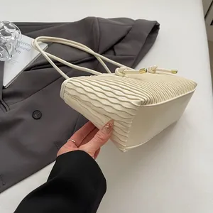 Detail of cream shoulder bag featuring unique wave pleats and gold drawstring accents