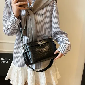 Detailed shot of a black glossy crossbody bag with silver buckle and woven shoulder strap