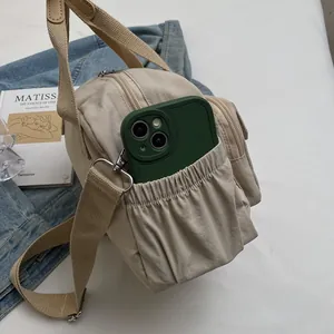 Detail view of cream nylon crossbody bag with multiple zip compartments and elastic side pocket