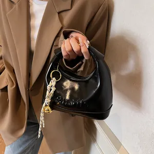 Detail of black glossy faux leather handbag with embossed letters and metal ball charm