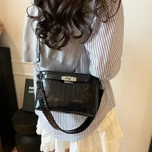 Detailed view of black patent leather crossbody bag with metallic buckle and woven strap