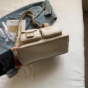 Detail of a beige nylon crossbody bag featuring dual front pockets and wide strap