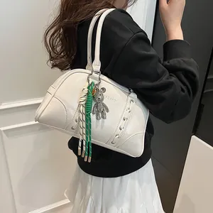 Close-up of beige Boston bag with YAZIANDI logo and bear charm with tassel detail