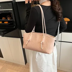 Detail of pink wavy pleated shoulder bag with knotted straps worn by a model in a kitchen