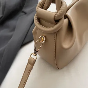 Detailed macro view of beige leather pleats and gold-tone metal lobster clasp on handbag