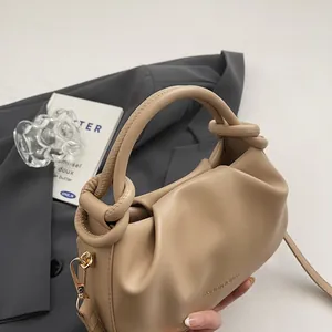 Detail of beige pleated handbag featuring knotted handle and gold metal hardware hooks