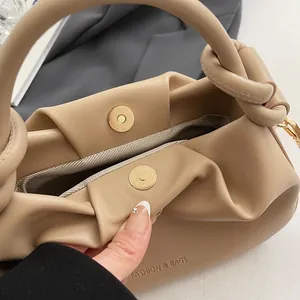 Detail of beige pleated handbag featuring a knotted handle and magnetic snap closure
