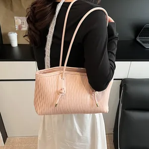 Detail of light pink shoulder bag featuring ripple texture and knotted straps with gold accents