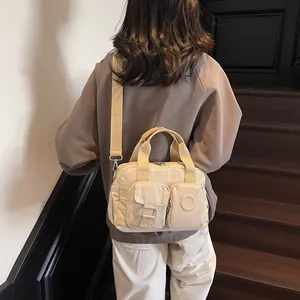 Close-up of cream nylon tote bag featuring front utility pockets and embossed logo
