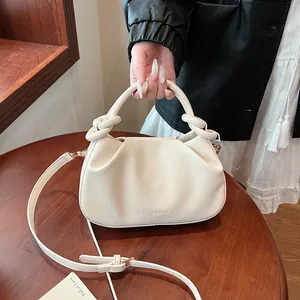 Close-up of cream pleated cloud bag with knotted handles and adjustable strap on a wood table