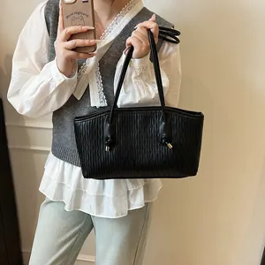 Detail of black tote bag with wave pleated texture and elegant gold-tipped knotted straps