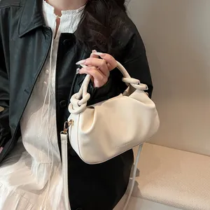 Detail view of cream pleated handbag with knotted handle and adjustable shoulder strap