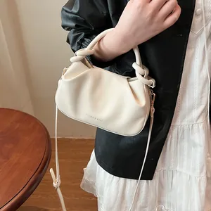 Close-up of beige pleated crossbody bag with knot handle and adjustable strap worn by model