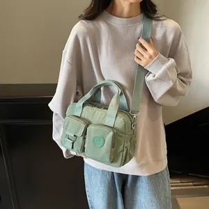 Detail of light green multi-pocket nylon bag featuring fashion logo and shoulder strap