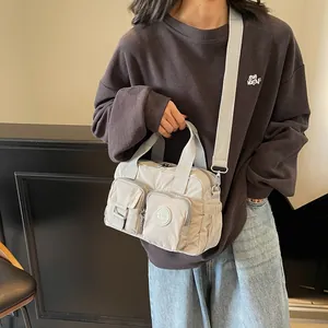 Detailed view of light gray multi-pocket nylon crossbody bag worn by model with wide strap