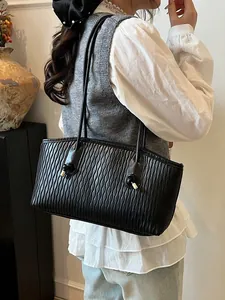 Black tote bag with wave pleated texture and gold metal accents shown on shoulder